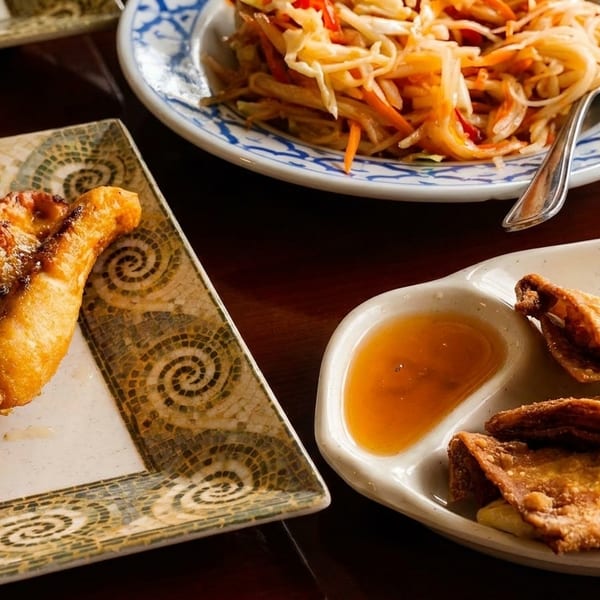 Three plates of Thai appetizers: chicken satay, papaya salad, and fried wontons with dipping sauce.